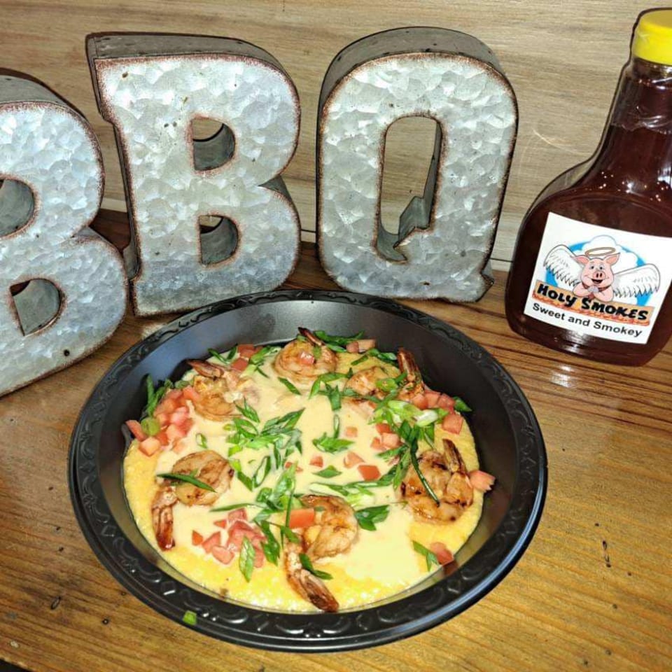 Shrimp and grits with diced tomatoes and green onions, next to a Holy Smokes BBQ sauce bottle.