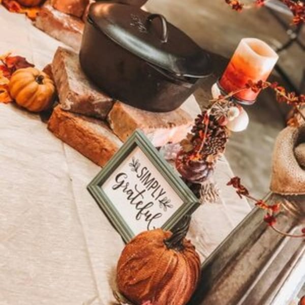 Autumnal decor with a cast iron pot, pumpkins, a candle, and a "Simply Grateful" sign.