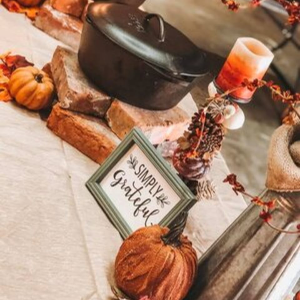 Autumnal decor with a cast iron pot, pumpkins, a candle, and a "Simply Grateful" sign.