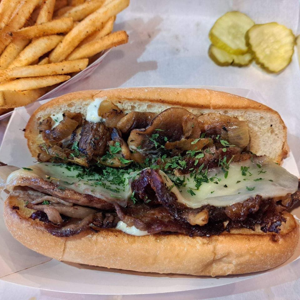 Holy Smokes BBQ's cheesesteak sandwich with fries and pickles on a white tray.