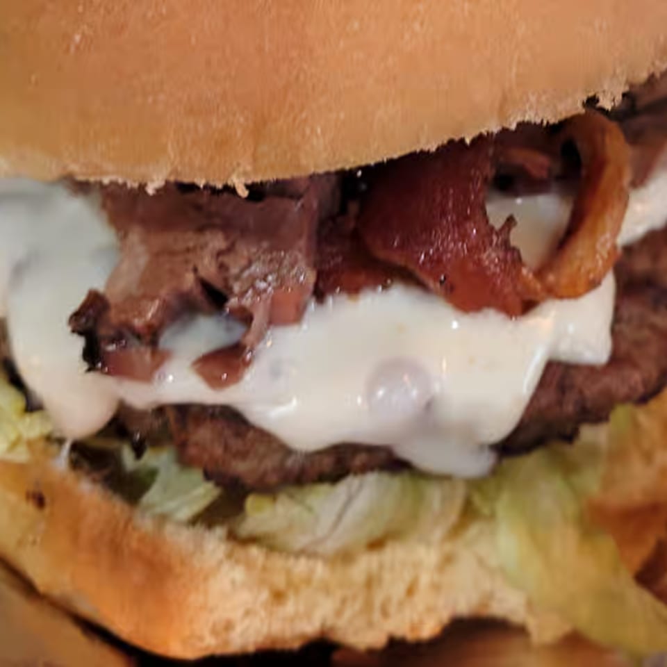 Close-up of a Holy Smokes BBQ burger with a patty, bacon, white sauce, and lettuce.