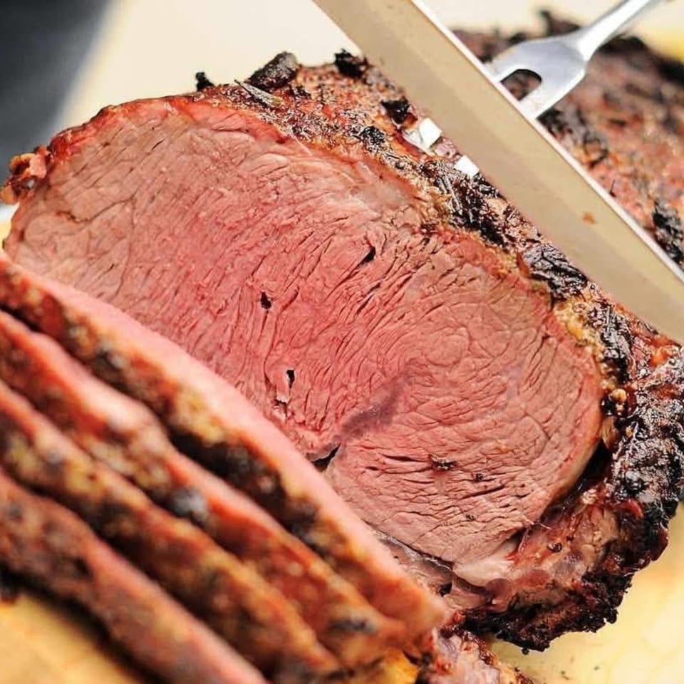 A knife slicing into a large, perfectly cooked Holy Smokes BBQ brisket with a pink interior.