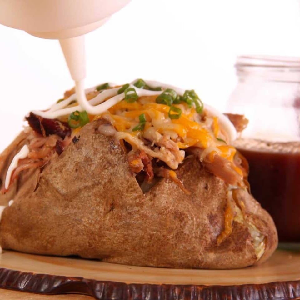 A baked potato overflowing with Holy Smokes BBQ pulled pork, cheese, green onions, and sour cream.