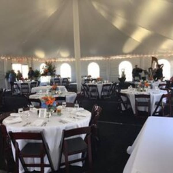 A large white event tent with round tables, chairs, and floral centerpieces, set for a Holy Smokes BBQ event.