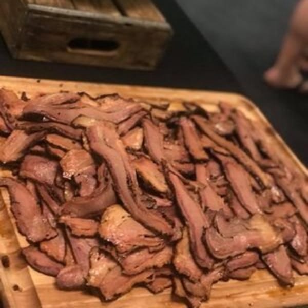 A large wooden platter overflowing with thinly sliced, tender Holy Smokes BBQ brisket.