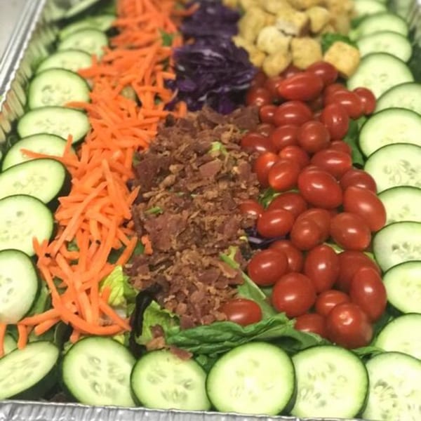 A catering tray of Holy Smokes BBQ salad with cucumbers, carrots, bacon bits, tomatoes, and croutons.
