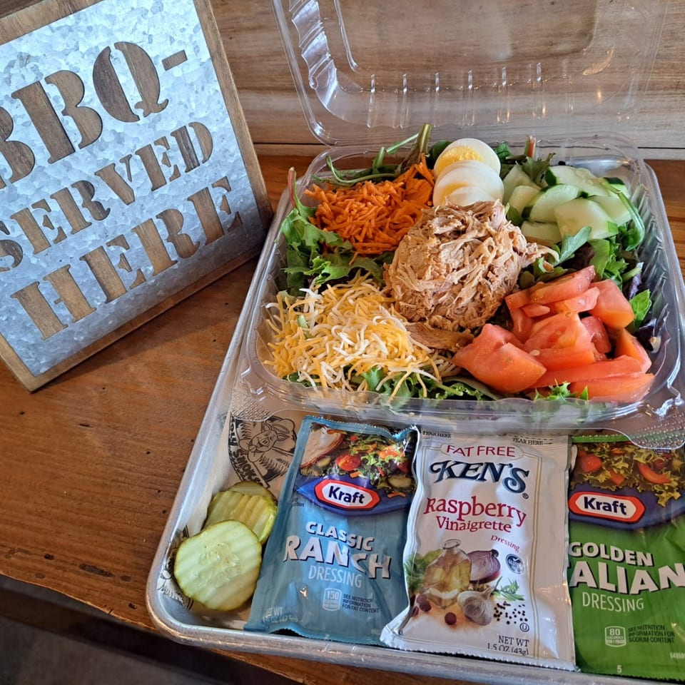 A Holy Smokes BBQ salad with pulled chicken, cheese, vegetables, and dressing packets.