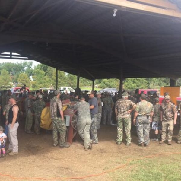 A large group of people in camouflage clothing gathered under a dark pavilion at an outdoor event.